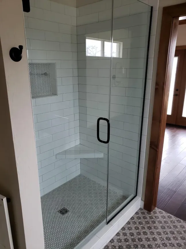 Glass shower with white subway tile, mosaic floor, and black handle in a bathroom