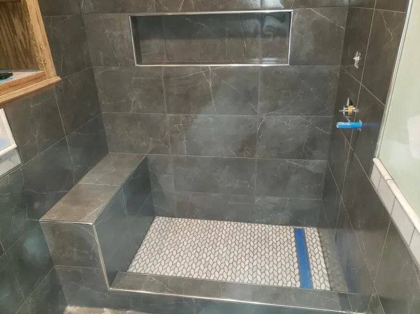 Empty tiled walk-in shower with built-in bench and drain.