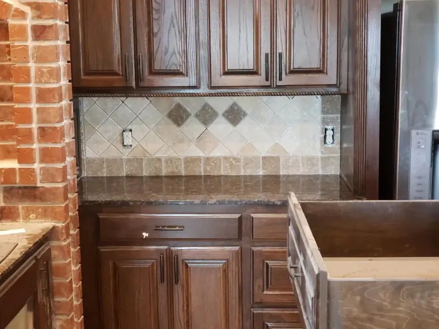 Empty kitchen with dark wood cabinets, beige tile backsplash, and stainless steel refrigerator.