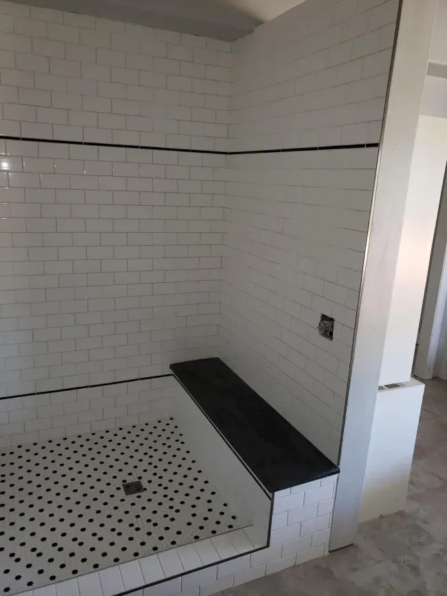 White tiled shower with black mosaic floor and a built-in black bench.
