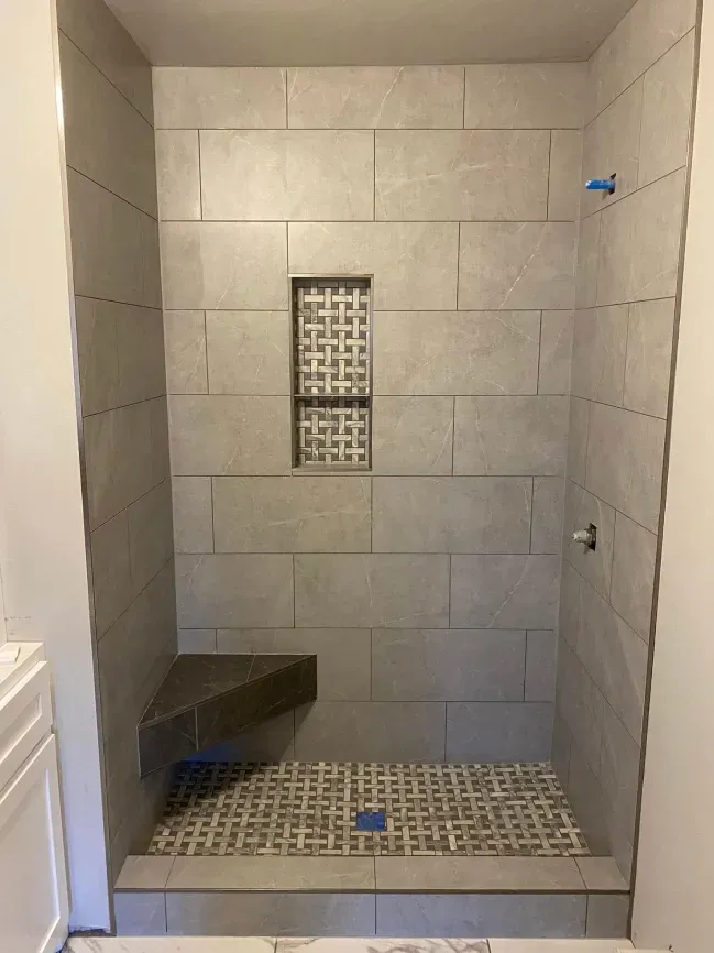 Empty tiled shower stall with built-in bench and central drain in a bathroom