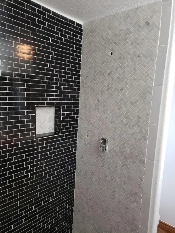 Bathroom shower wall with black tile, gray tile, niche, and plumbing fixture