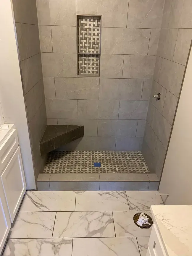 Small tiled walk-in shower with a bench and a wall niche, shown from the bathroom doorway.
