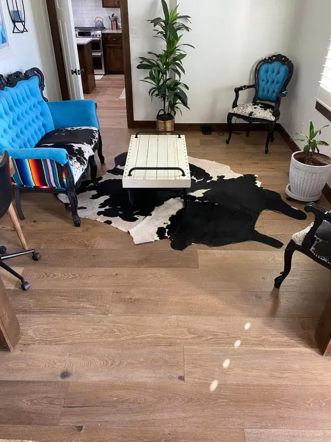Living room with blue chairs, white table, potted plants, and a black-and-white cowhide rug on wood floor