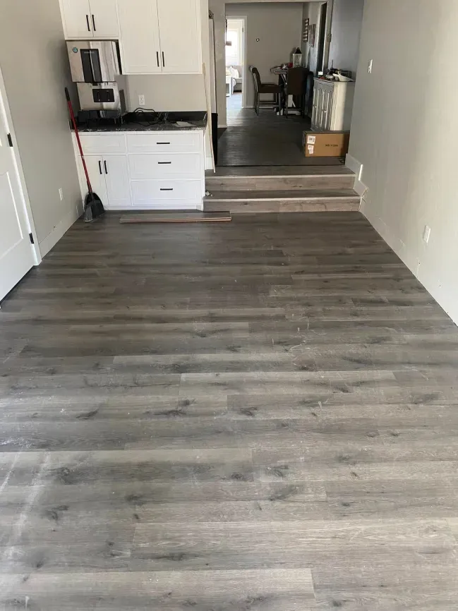 Empty apartment room with gray wood floors, white cabinets, and a step up to a back room