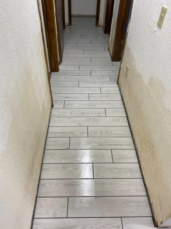 Narrow hallway with light wood plank flooring and beige walls leading to doorways.