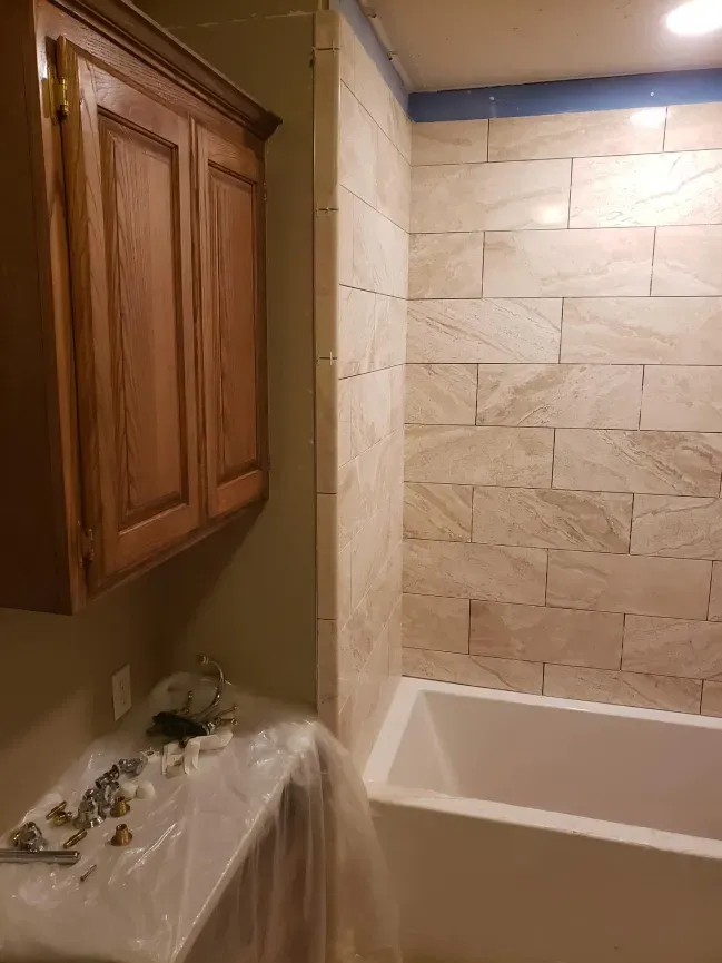 Small bathroom with wood cabinet, sink covered in plastic, and a tiled shower tub.