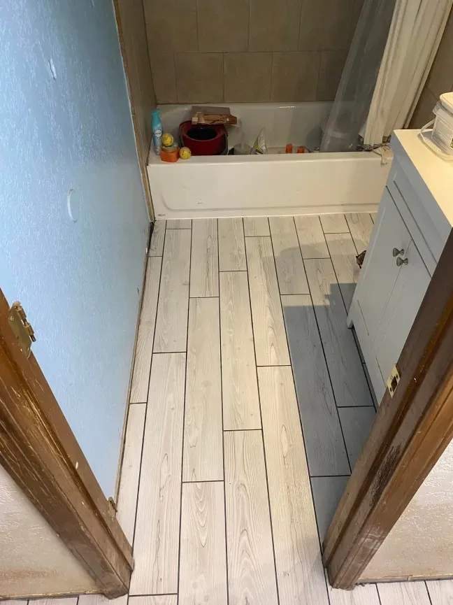 Bathroom with white painted floorboards, a bathtub, and a cabinet in a narrow doorway view