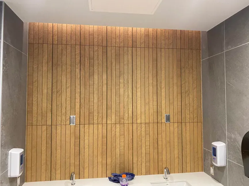 Public restroom with wooden stall doors and gray tile walls, sinks visible at the bottom.