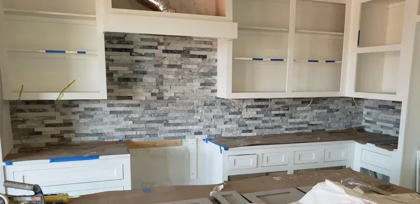 Modern kitchen with white cabinets, gray tile backsplash, and unfinished countertop area under renovation