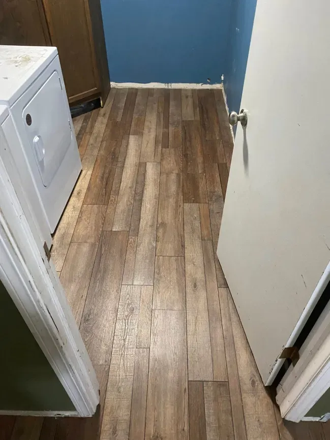 Narrow hallway with wood-look flooring, white doors, blue wall, and a small laundry closet on the left.