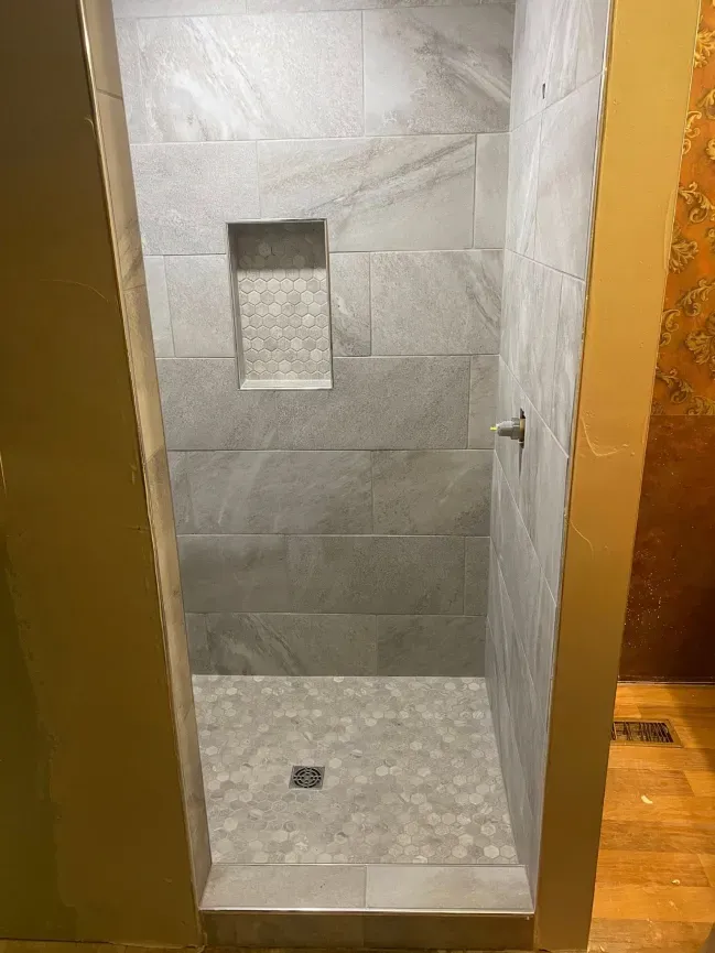 Walk-in shower with gray tile, built-in niche, and pebble-look floor drain in a bathroom.