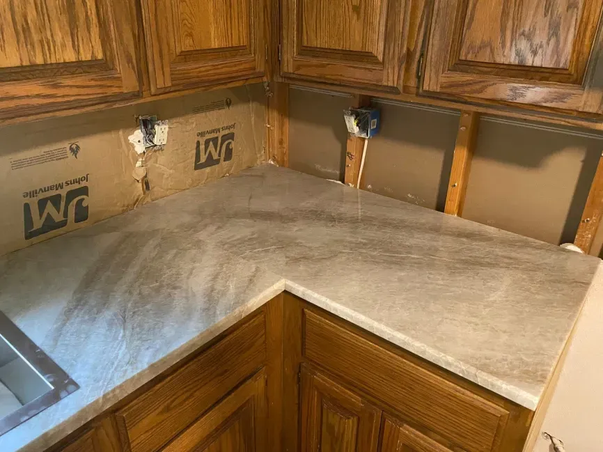 Corner kitchen countertop under construction with unfinished backsplash and exposed wall studs