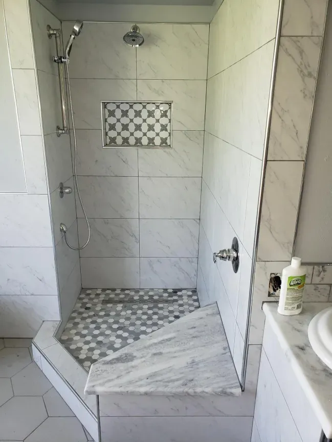 Walk-in shower with white tile, built-in shelf, and a gray mosaic floor tile section
