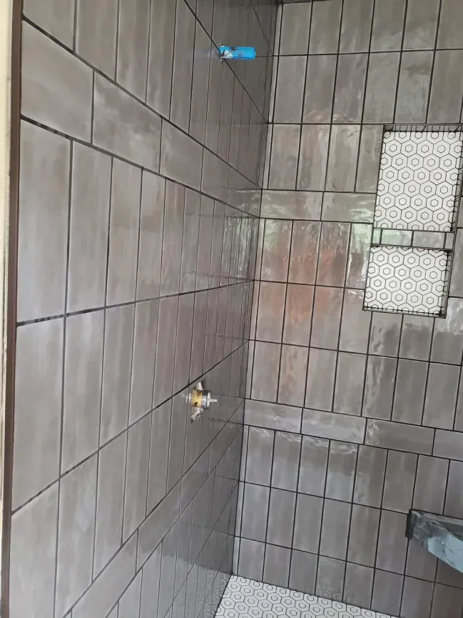 Tiled bathroom shower with a wall-mounted faucet and small window.