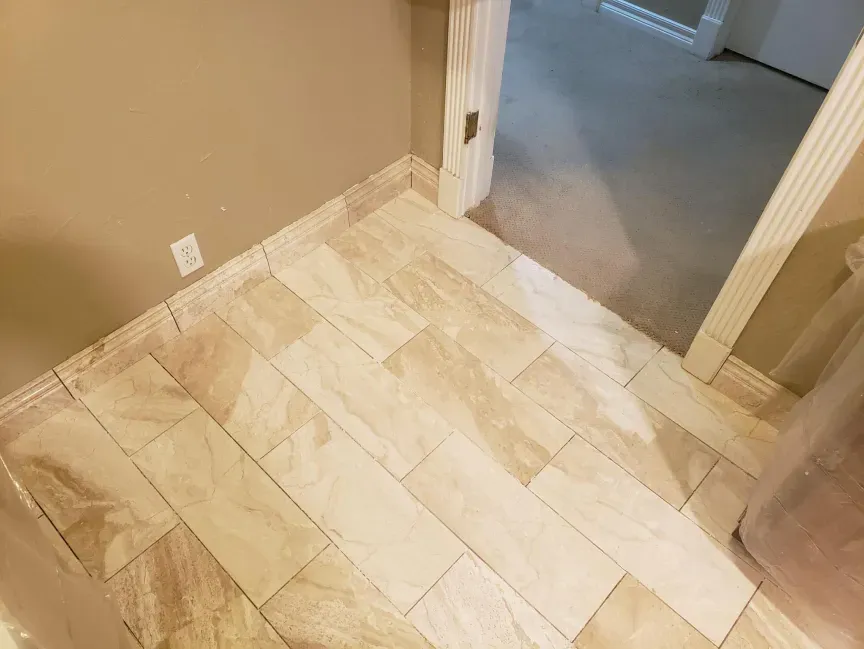 Beige tiled floor at a doorway between a carpeted room and a hallway.