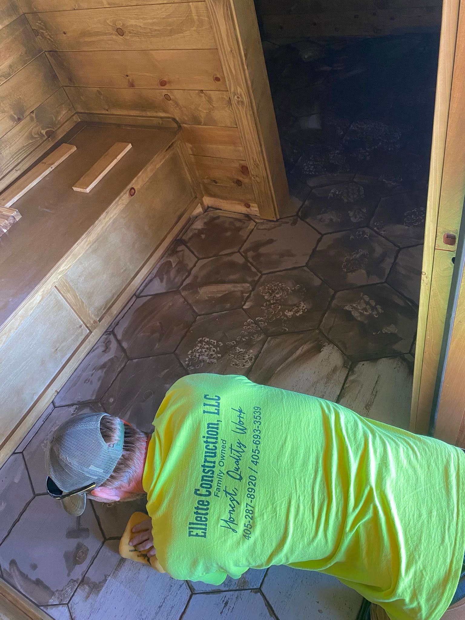 Person in bright green shirt kneels on a wooden floor, working near a chest and doorway.