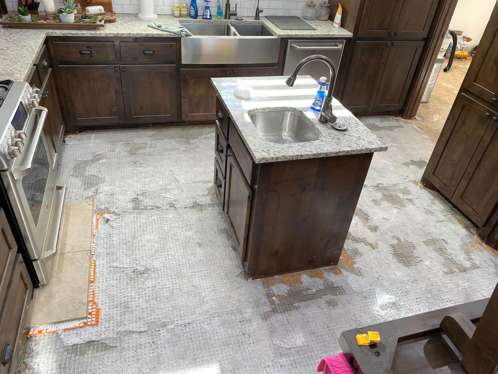 Kitchen under renovation with dark cabinets, center island, sink, and unfinished floor covering