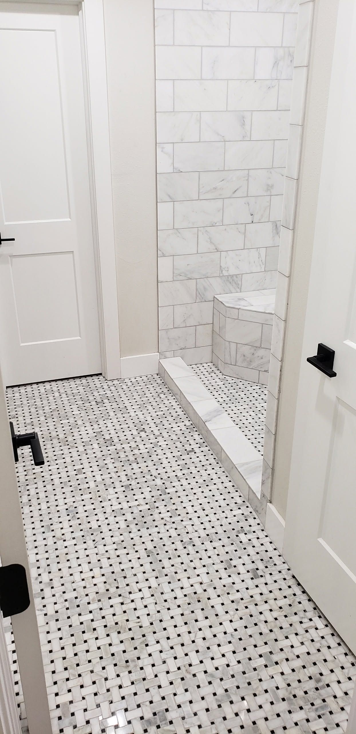 Narrow tiled bathroom with white doors, a shower nook, and a black-and-white mosaic floor.
