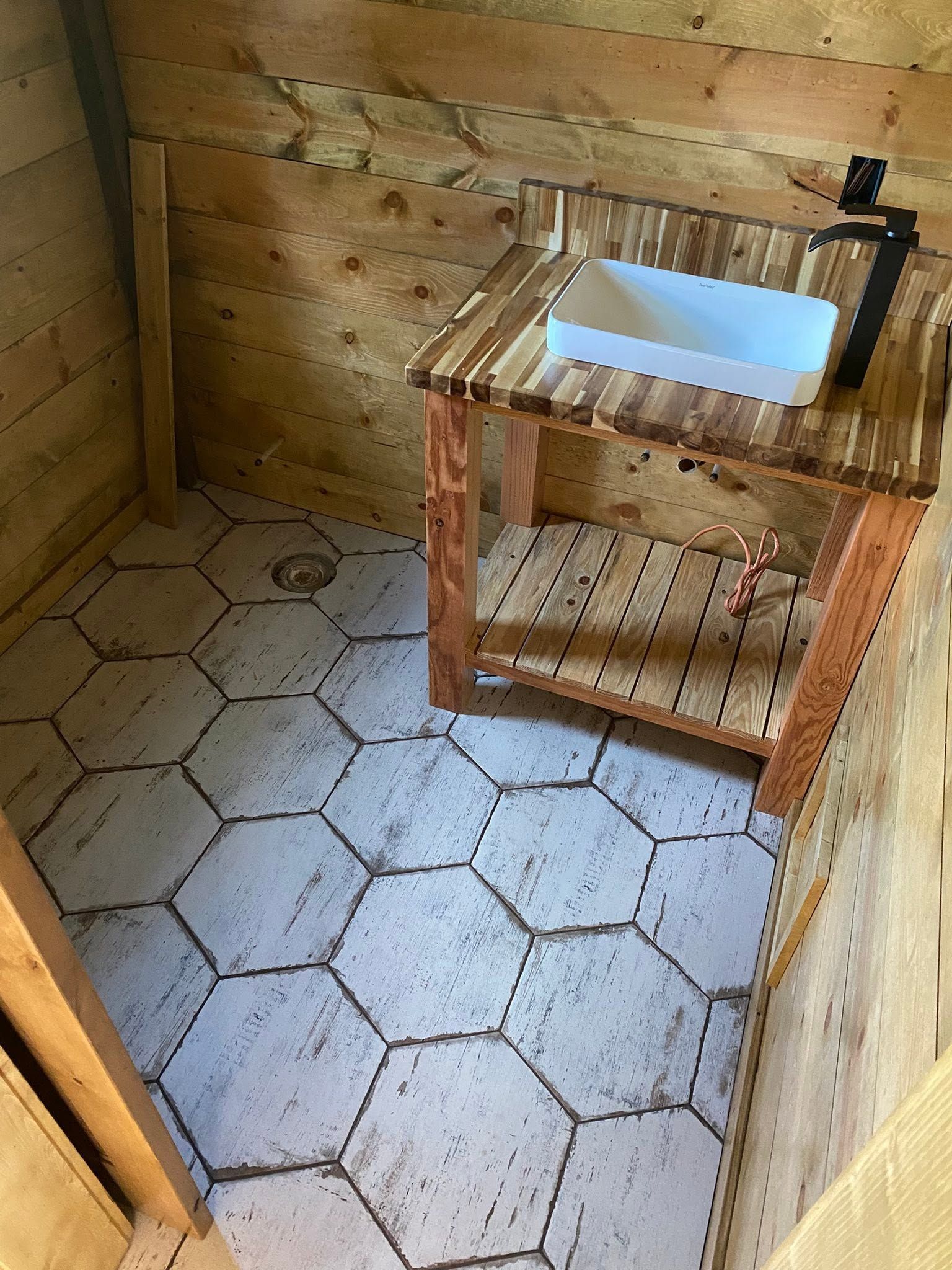 Small wooden bathroom with hexagon tile floor and a sink on a rustic wooden stand.