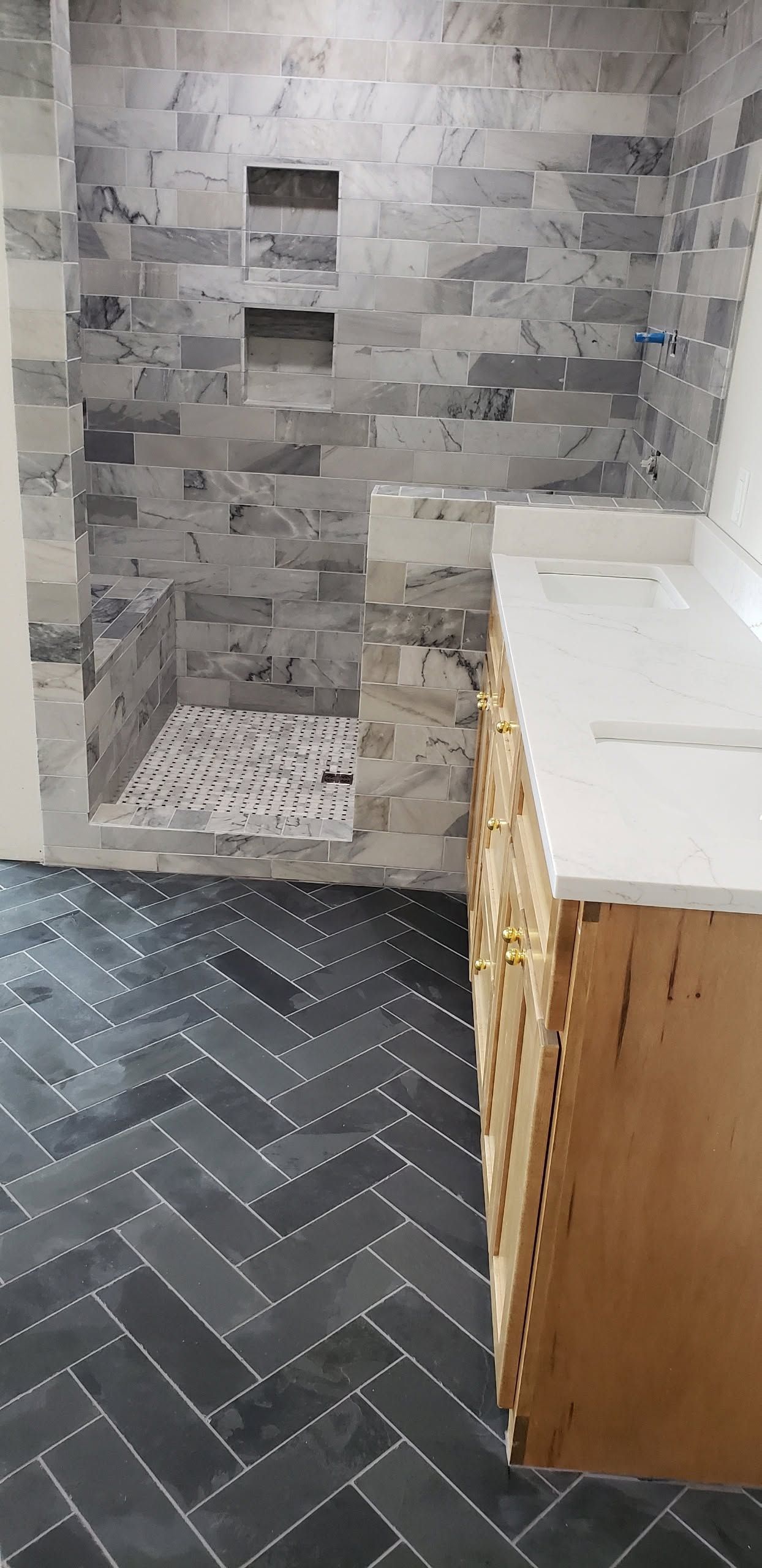 Small tiled bathroom under renovation with a white vanity, gray wall tiles, and dark herringbone floor.