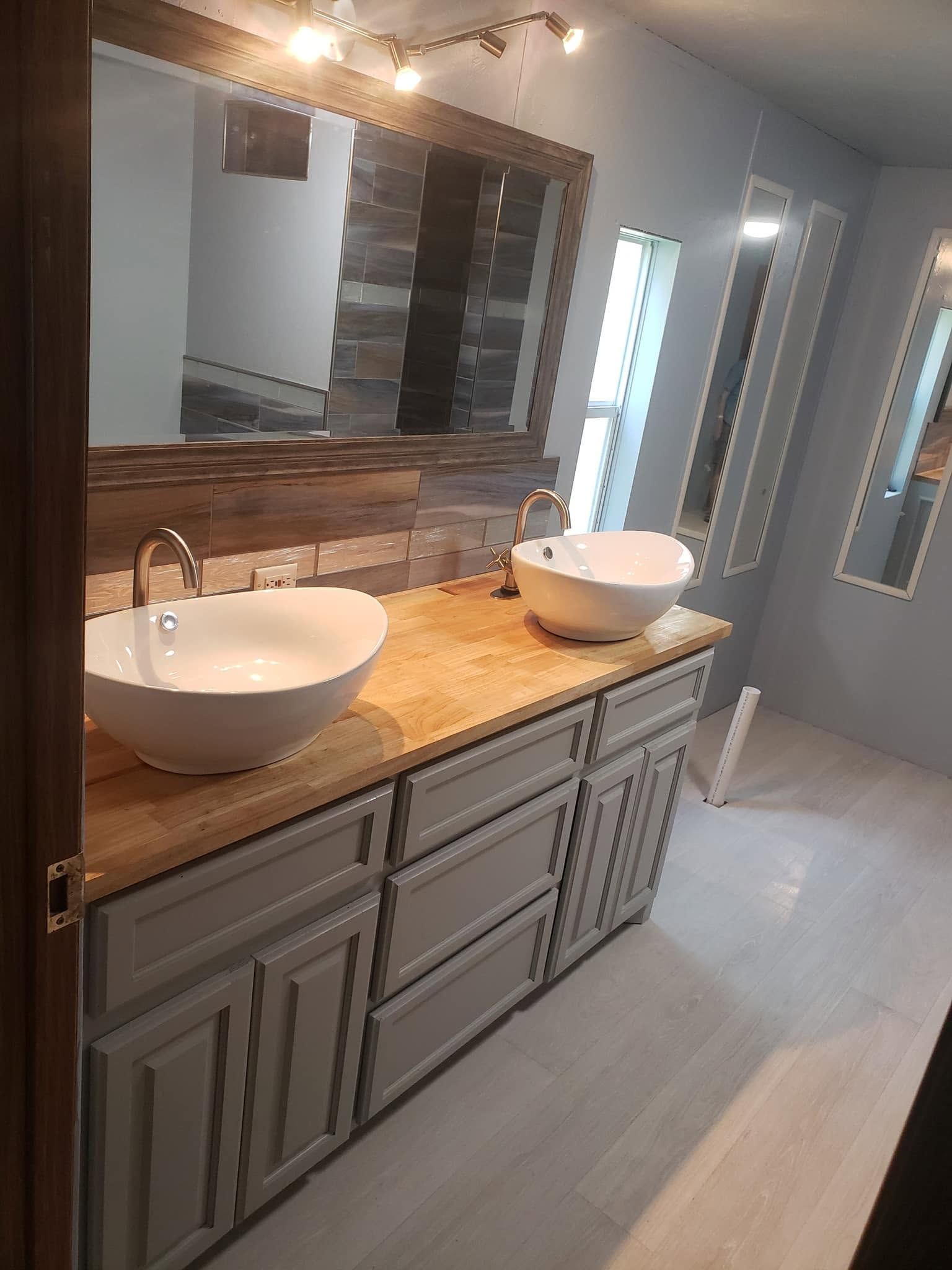 Modern bathroom vanity with double white sinks, gray cabinets, wood countertop, and large mirror.