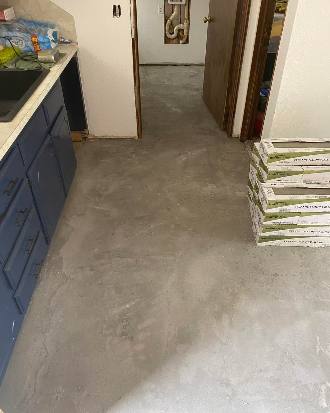 Concrete floor in a hallway under renovation, with blue cabinets on the left and stacked materials on the right.