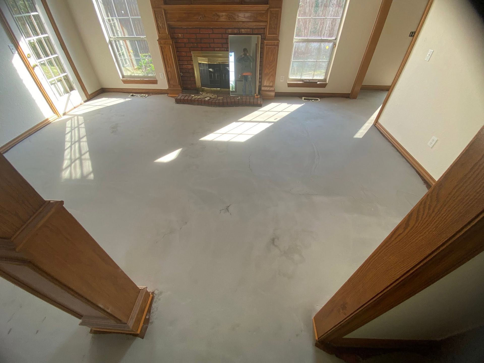 Sunlit empty living room with fireplace, windows, and bare carpeted floor
