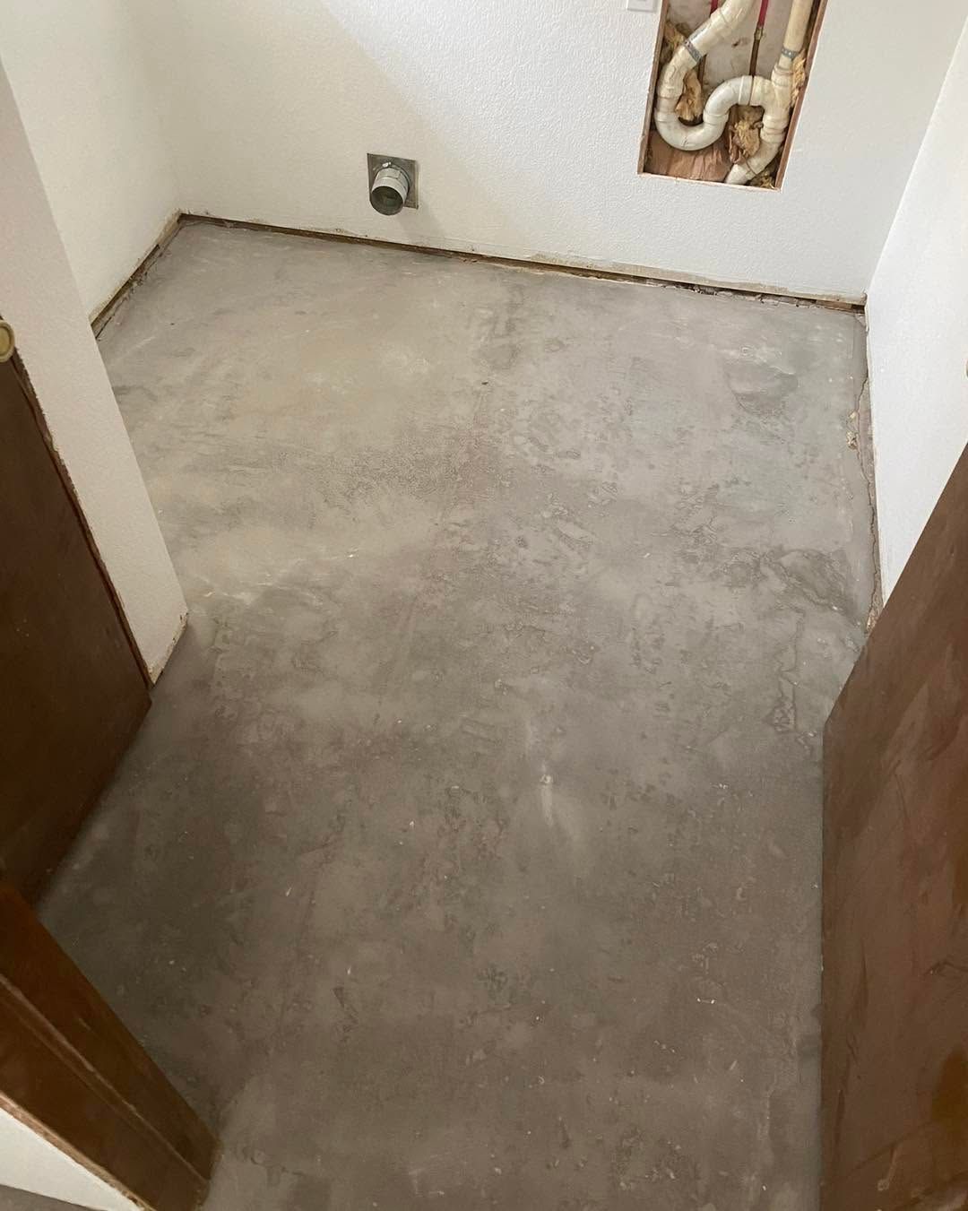 Empty unfinished room with bare gray concrete floor and white walls, viewed from the doorway.