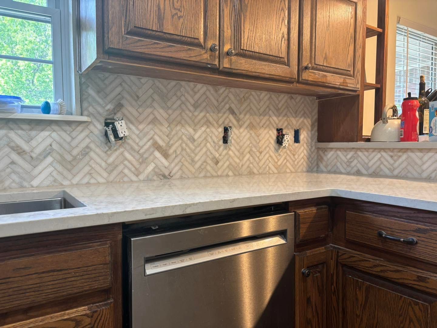 Modern kitchen counter with herringbone backsplash, stainless dishwasher, and wooden cabinets
