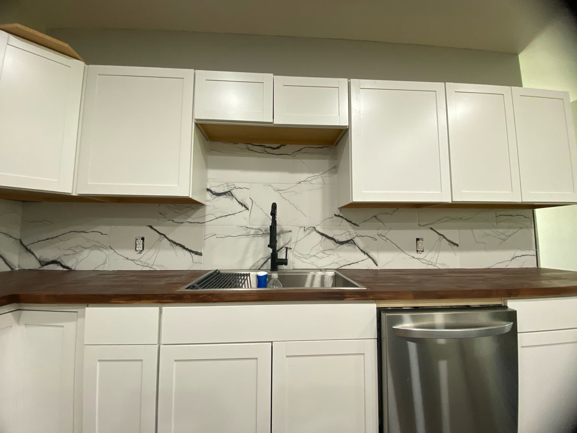Modern white kitchen with marble backsplash, wood countertop, and stainless-steel dishwasher