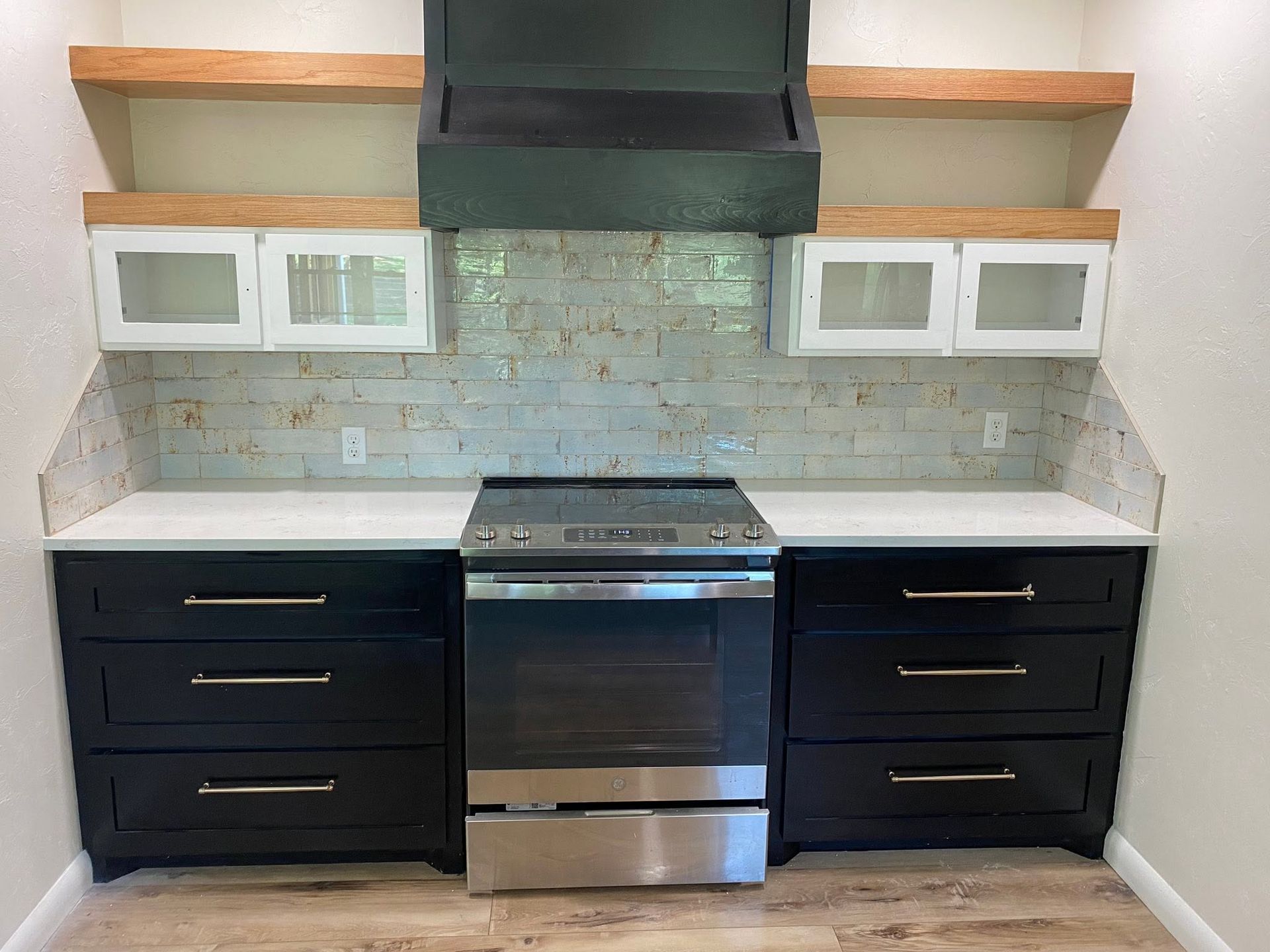 Modern kitchen with black cabinets, stainless steel stove, white countertops, and glass-front wall cabinets.