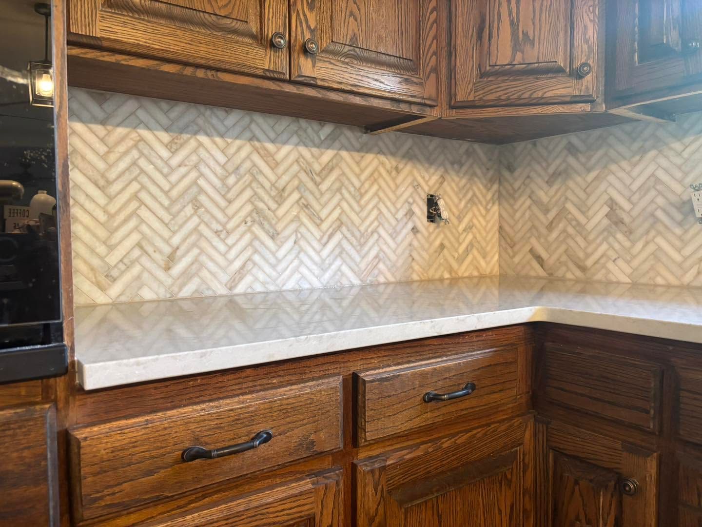 Kitchen countertop with herringbone tile backsplash and wooden cabinets