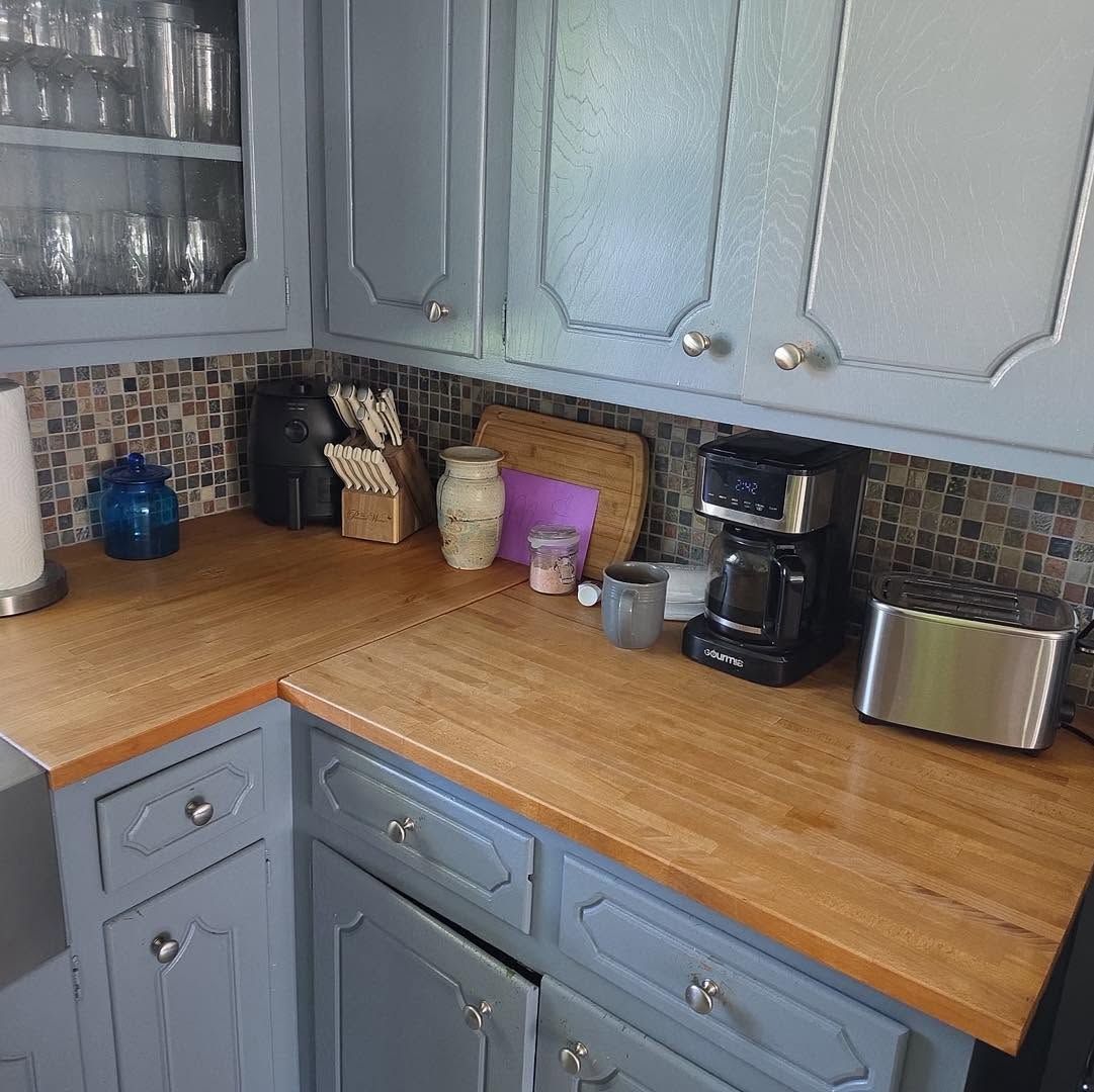 Blue-gray kitchen corner with wooden countertops, coffee maker, toaster, and jars on the counter.