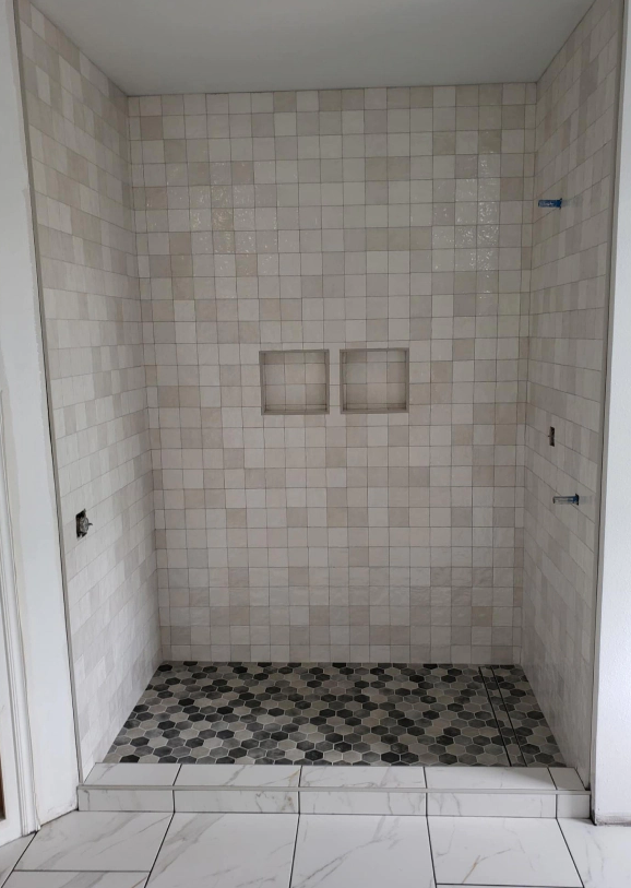 Empty tiled shower alcove with two square wall niches and patterned floor tiles