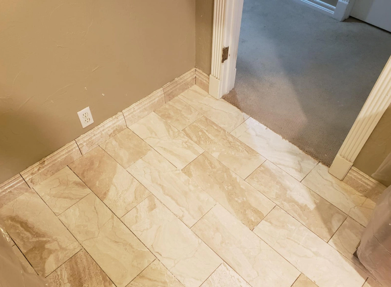 Light tan tiled floor at a doorway between rooms with beige walls and white trim