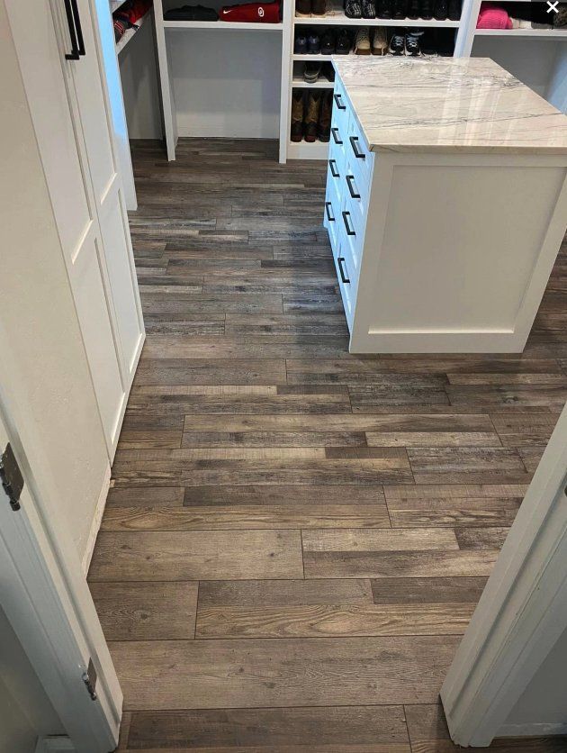 Empty kitchen hallway with gray wood flooring and white cabinets leading to a pantry area