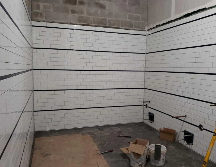 Empty tiled room under construction with white subway-tile walls and tools on the floor.