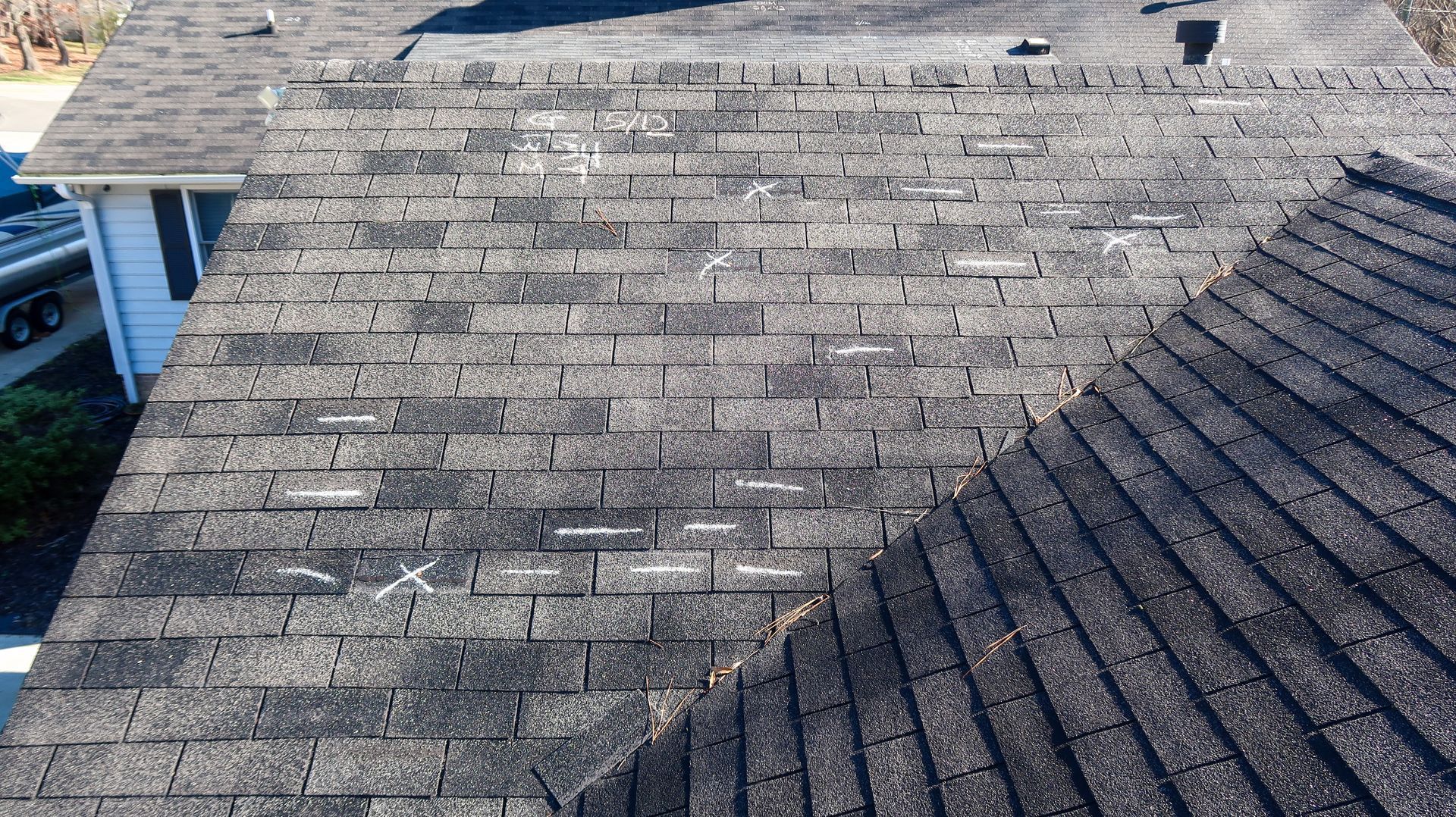 Close-up of a weathered shingled roof with patches of wear and sunlight shadow lines