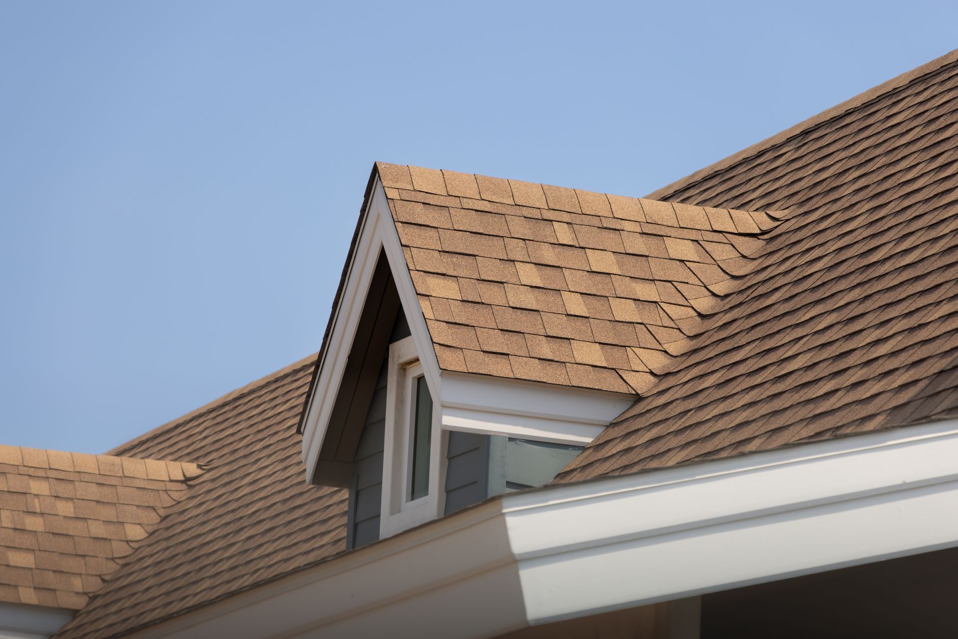 House roof with brown shingles and a small dormer window against a blue sky