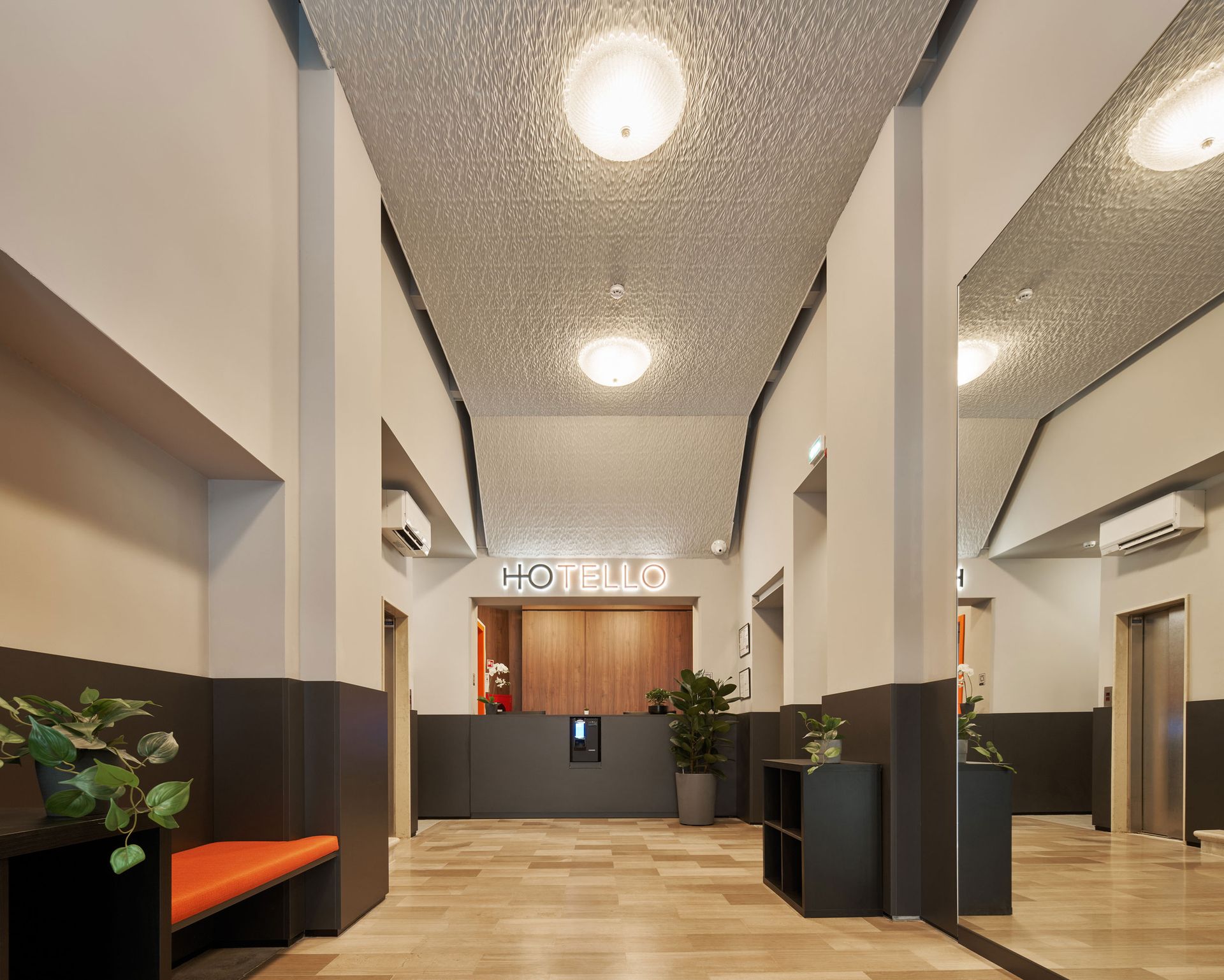 Hall di Hotello con soffitto strutturato, reception e zona salotto con panca arancione.