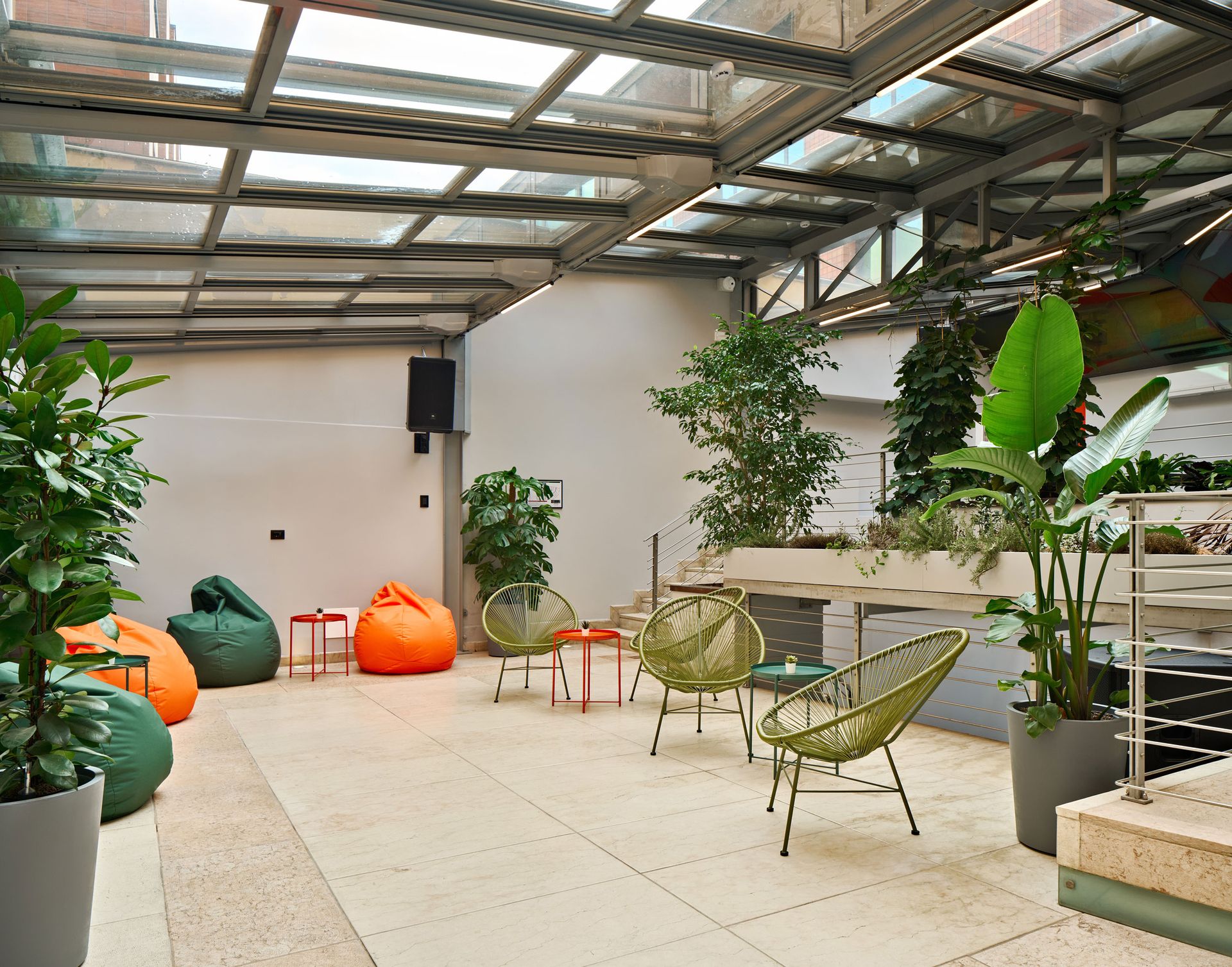 Un salotto esterno coperto con poltrone a sacco, sedie in filo metallico verde, piante in vaso e tavoli.