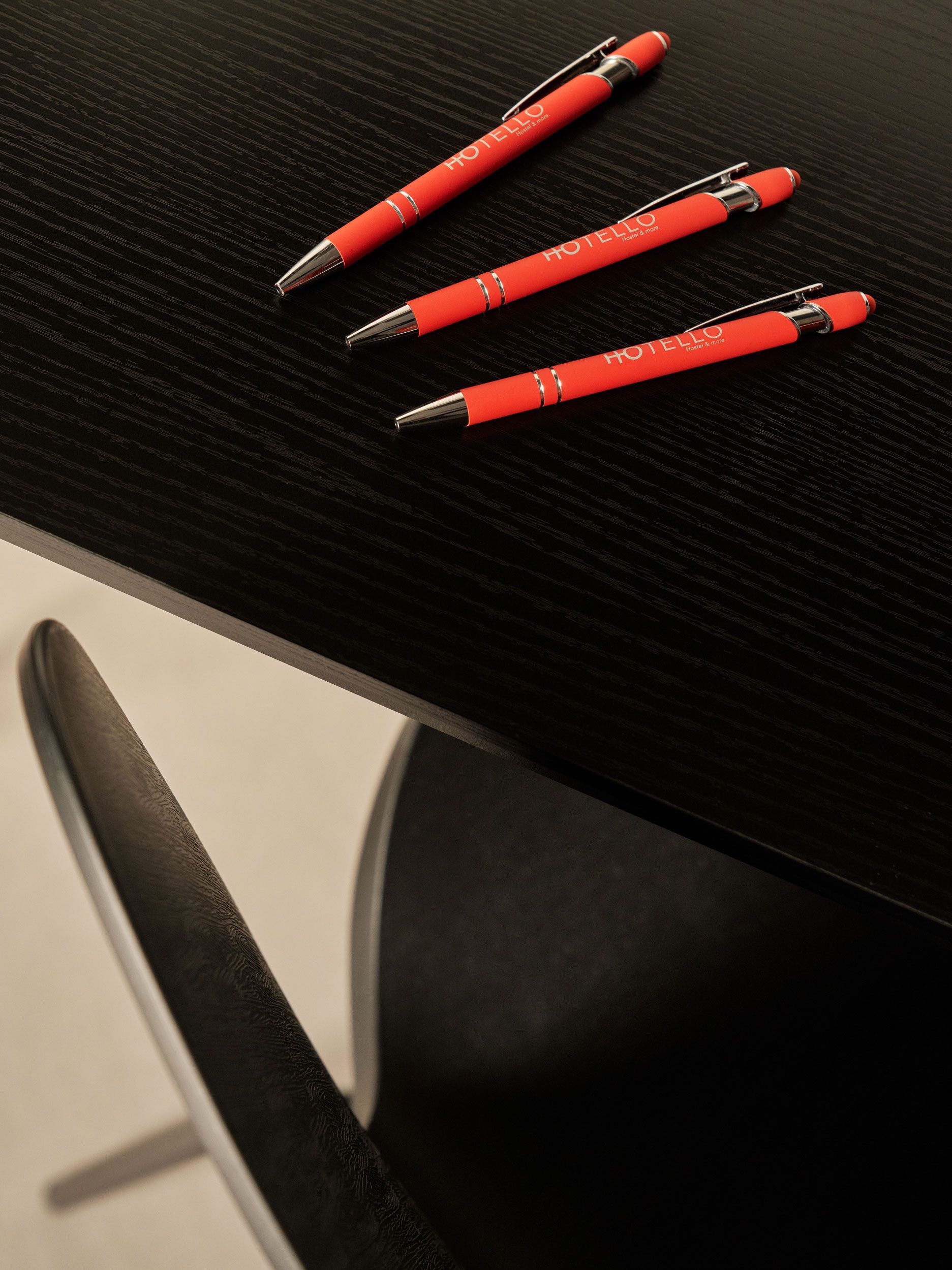 Tre penne rosse su un tavolo nero vicino a una sedia nera.