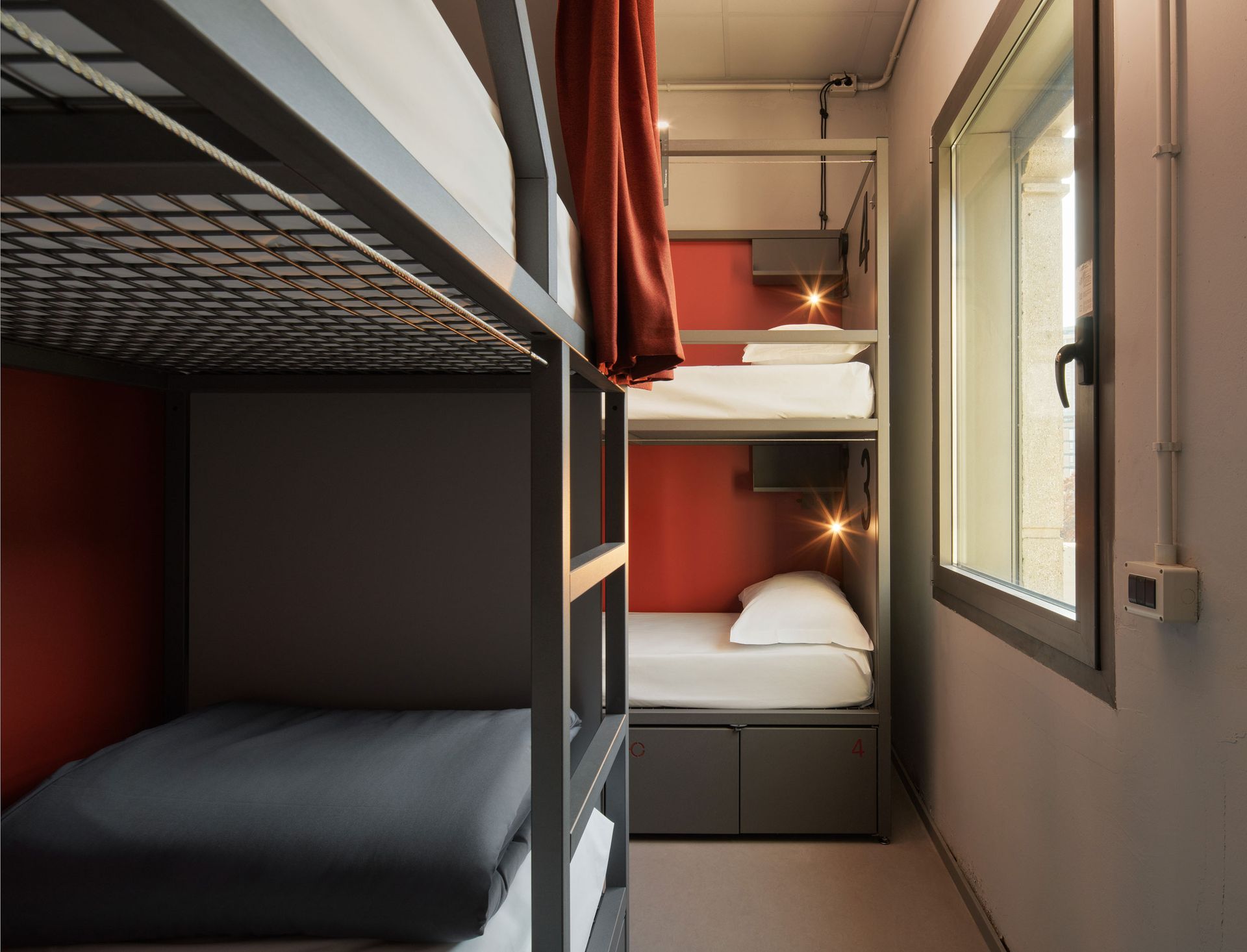 Letti a castello in una stanza di ostello con pareti decorate in rosso e una finestra.