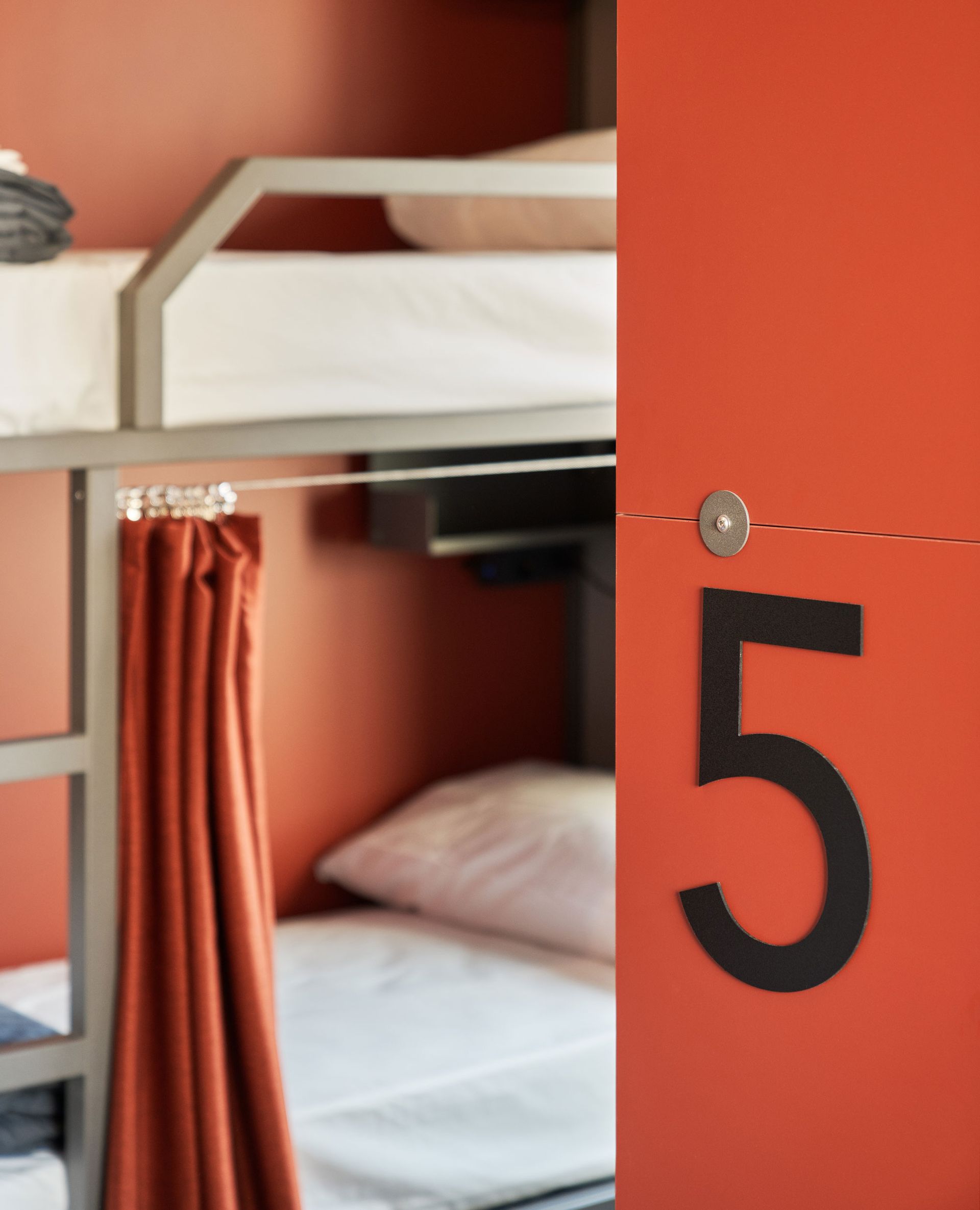 Stanza arancione con letti a castello; una porta con il numero 5.