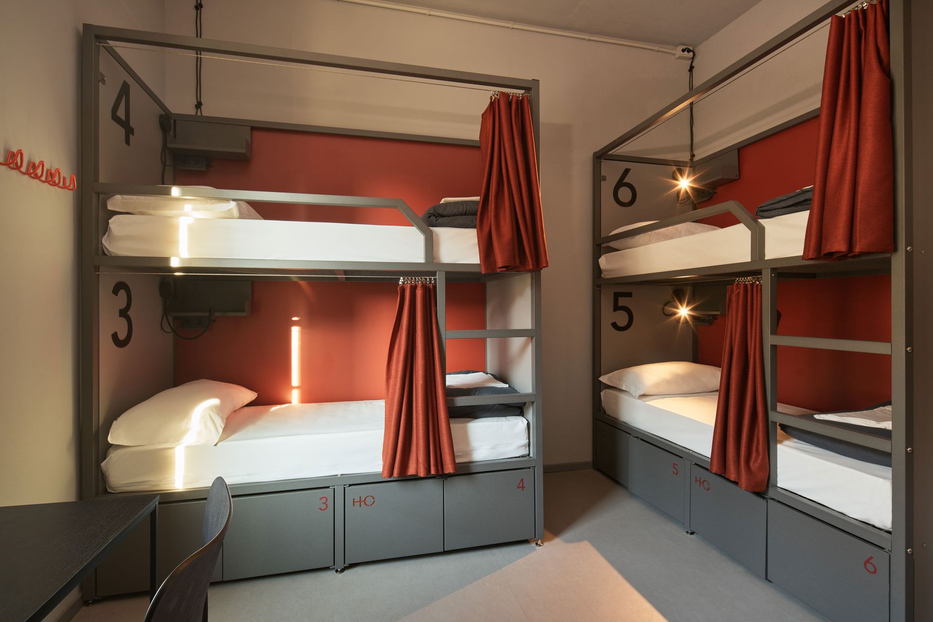 Letti a castello in una stanza di ostello con cuccette numerate, tende arancioni e spazio per riporre le cose.