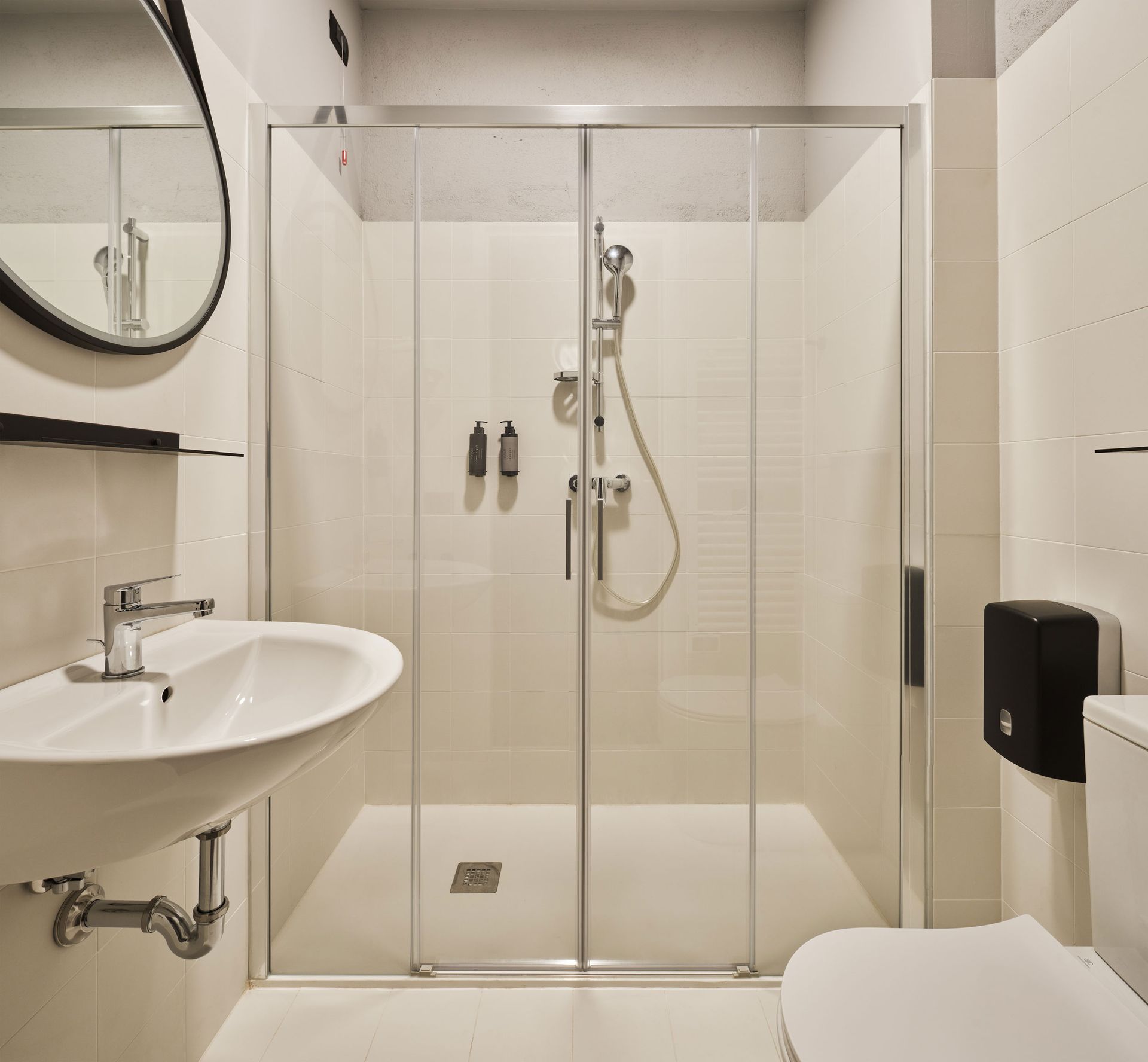 Bagno con doccia, lavabo e WC. Porte doccia in vetro beige e bianco. Specchio rotondo.