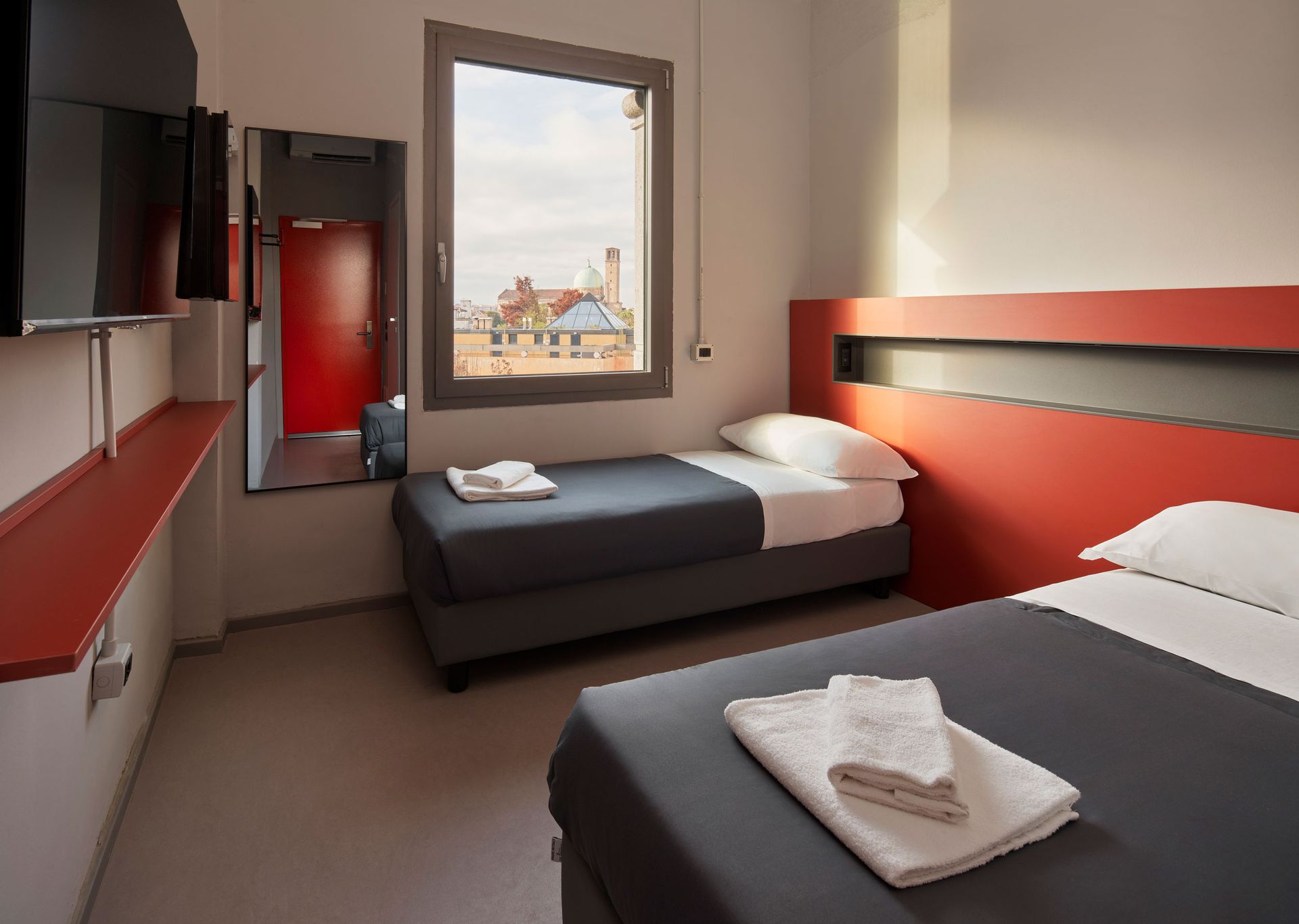 Twin beds in a modern hotel room with a window view of rooftops.