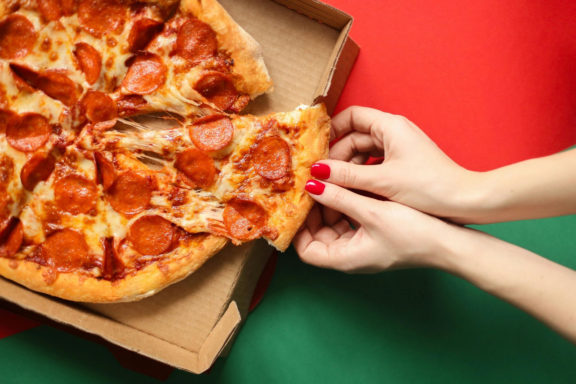 Una donna sta tirando fuori una fetta di pizza al salame piccante da una scatola.