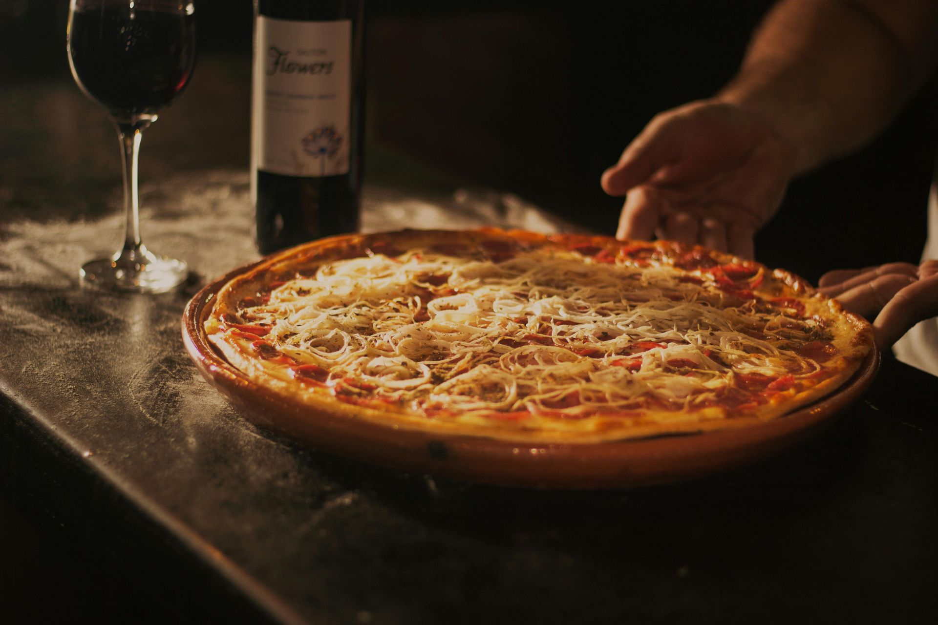 Una pizza è appoggiata su un tavolo accanto a un bicchiere di vino e una bottiglia di vino.